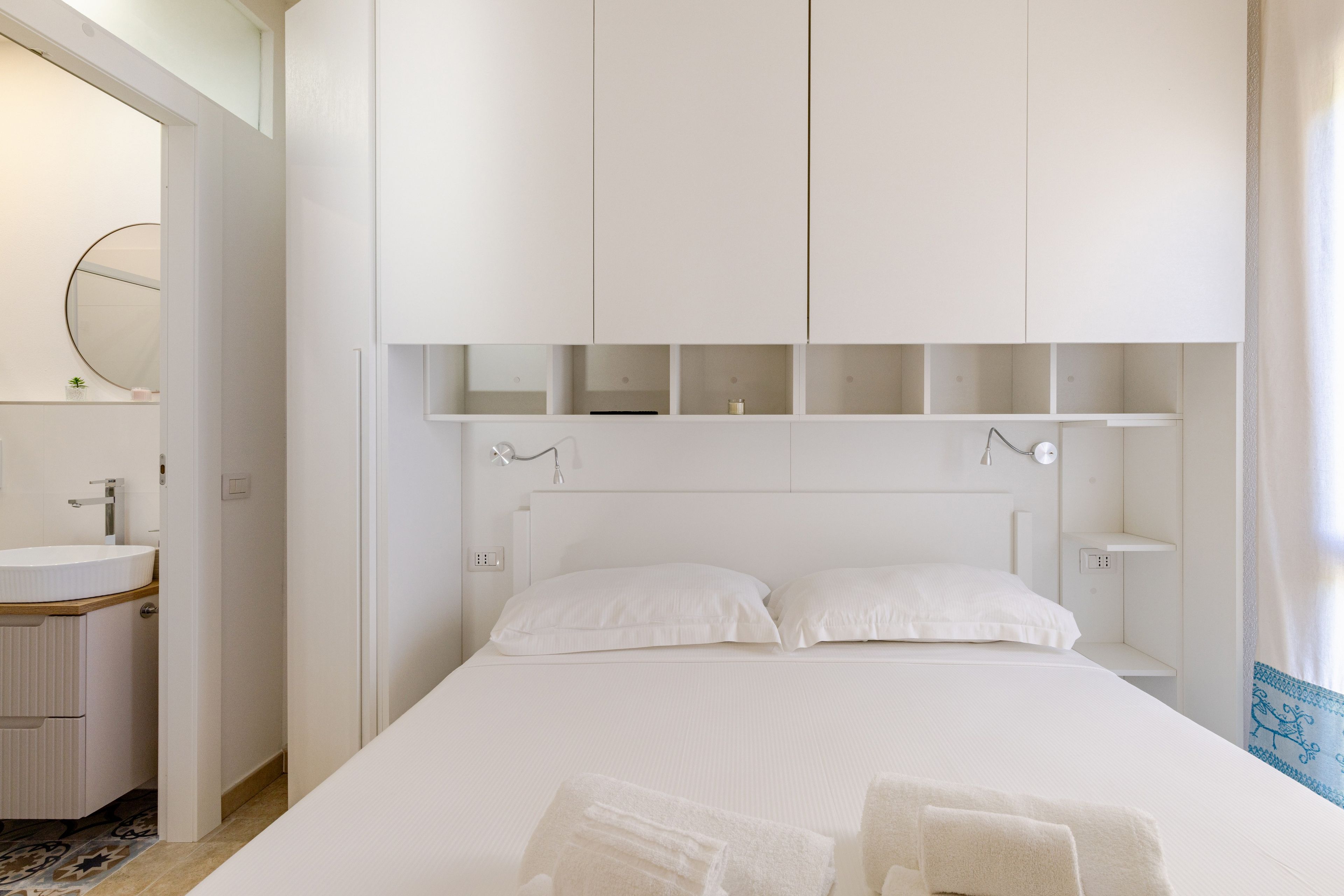 A hotel room with a large bed, a bedside table, a mirror, and a bathroom with a sink and toilet.