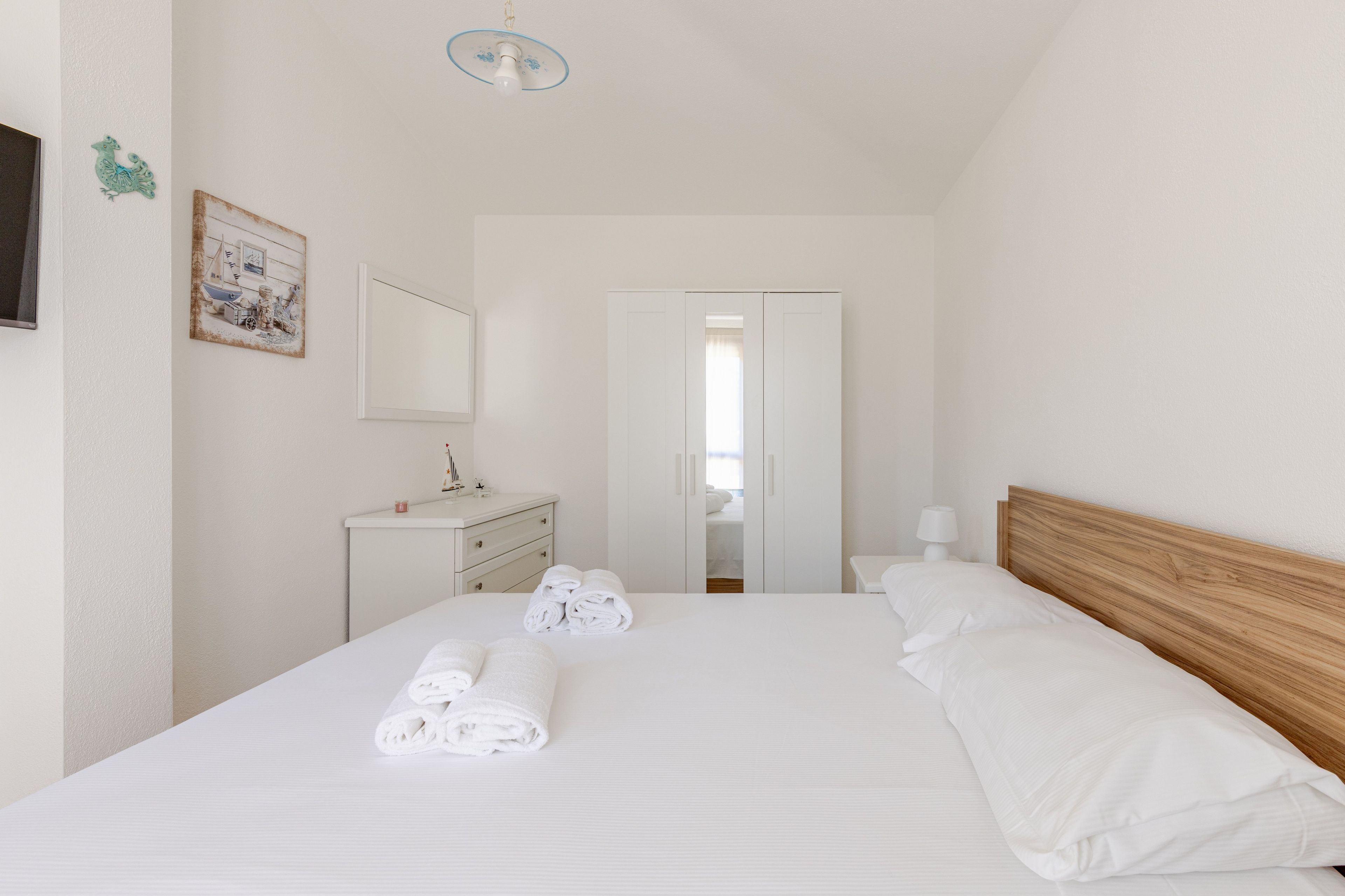 Una camera d'albergo con un letto, un comodino, una cassettiera, uno specchio e una porta che dà su un'altra stanza.