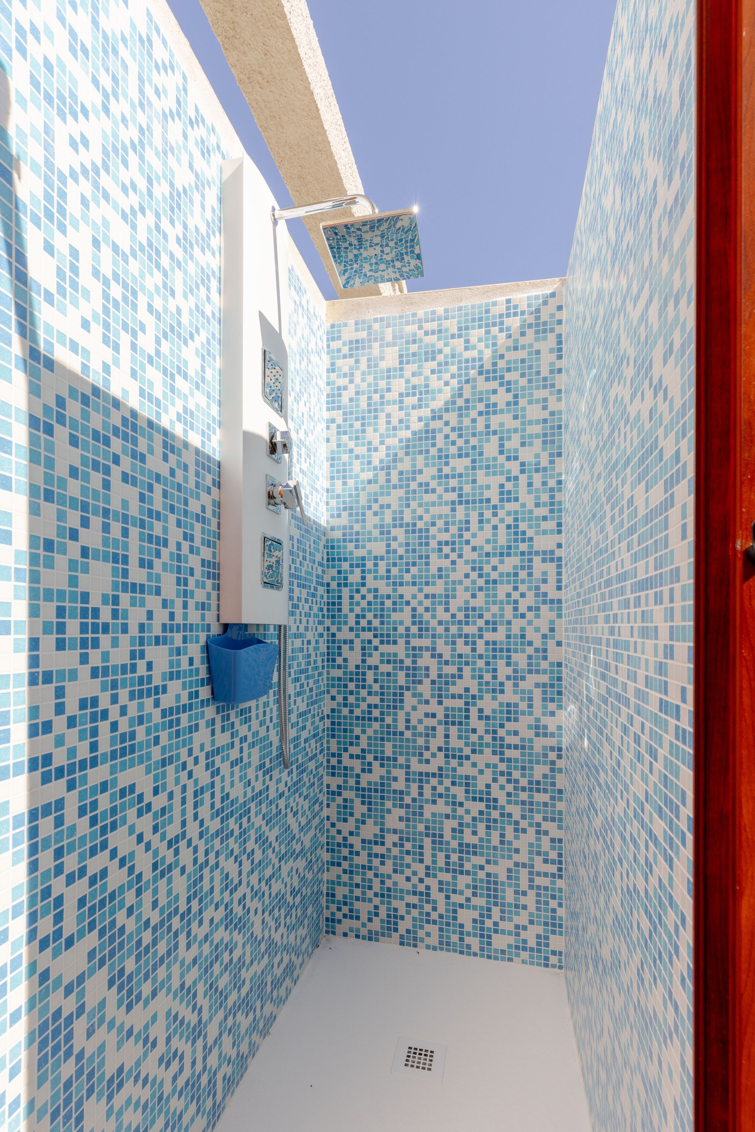 A small, tiled shower area with a white sink and a blue basin.