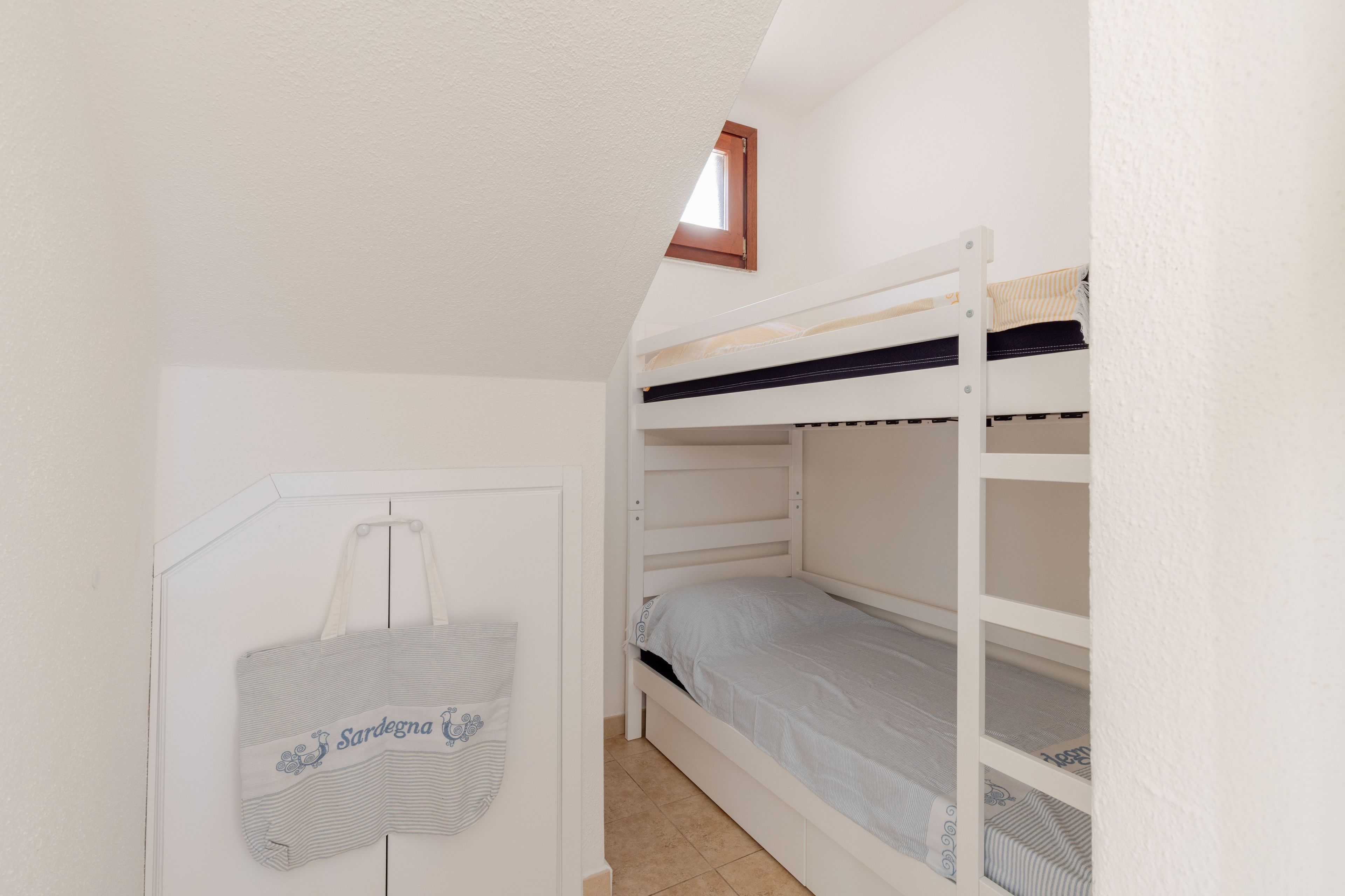 Ein Schlafraum mit Etagenbett, kleinem Fenster und Tür.