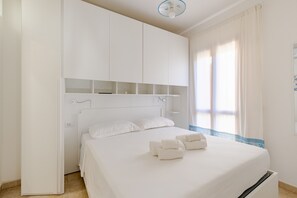 A bedroom with a bed, white curtains, and a ceiling light.