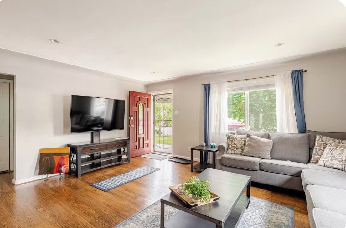 Una sala de estar moderna con un televisor de pantalla plana, un sofá, una mesa de centro y piso de madera.