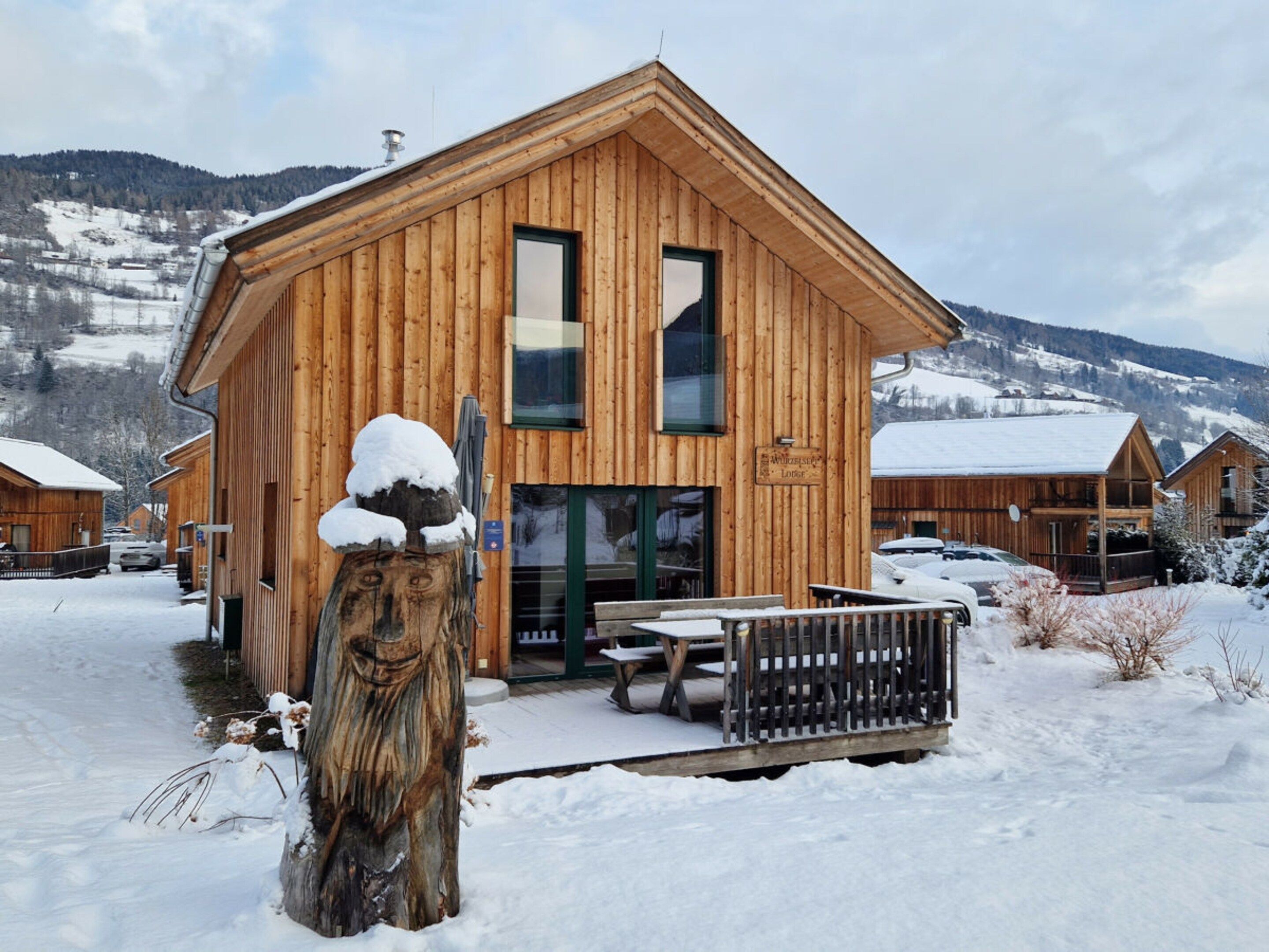 A wooden lodge with a large entrance, a wooden fence, and a snow-covered landscape.