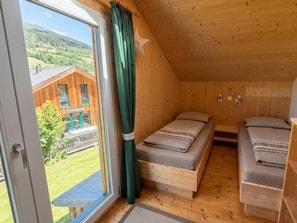 A wooden cabin with two beds, a window with curtains, and a view of a building outside. - Cabin With 1 Bedroom (Sankt Georgen am Kreischberg)