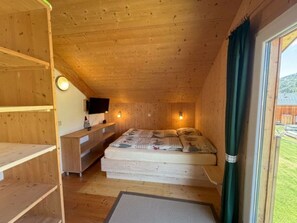 Ein Holzinnenraum mit einem Bett, einem Fernseher und einem Fenster mit Vorhängen.