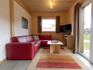 Ein gemütliches Wohnzimmer mit einem roten Sofa, einem kleinen Holztisch und einem an der Wand befestigten Fernseher.