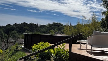 A wooden deck with a white chair, surrounded by greenery and overlooking a forested area.