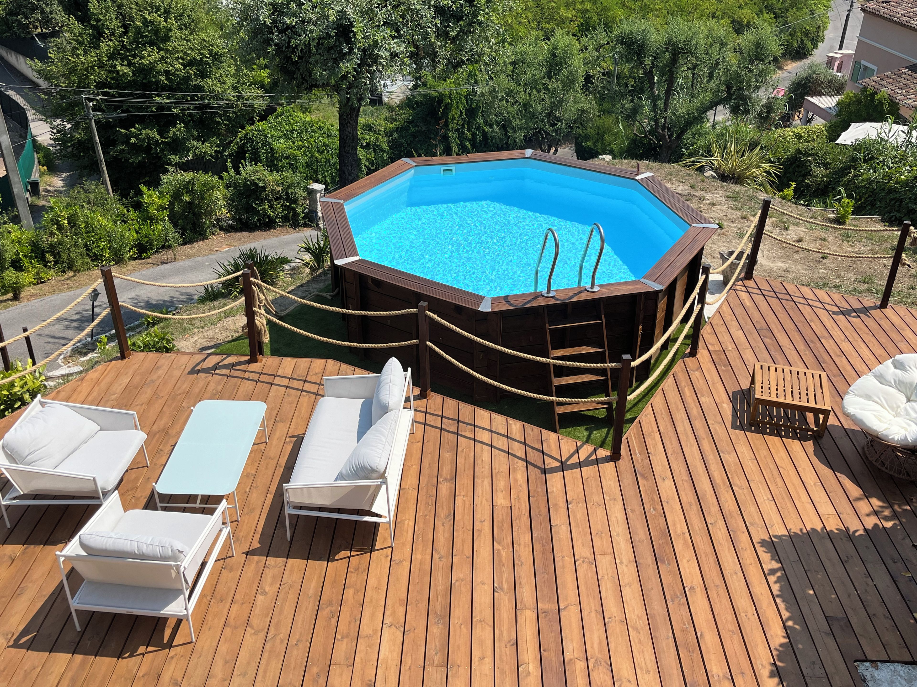 Eine Holzterrasse mit Swimmingpool, Liegestühlen und einem Geländer aus Seil.