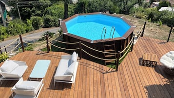 Eine Holzterrasse mit Swimmingpool, Liegestühlen und einem Geländer aus Seil.