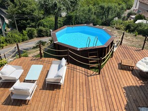 A wooden deck with a swimming pool, lounge chairs, and a rope barrier.