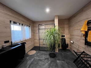 Ein modernes Badezimmer mit einer Holzvertäfelung, einem schwarzen Waschbecken, einer großen Topfpflanze und einem Handtuchhalter mit einem gelben Handtuch.