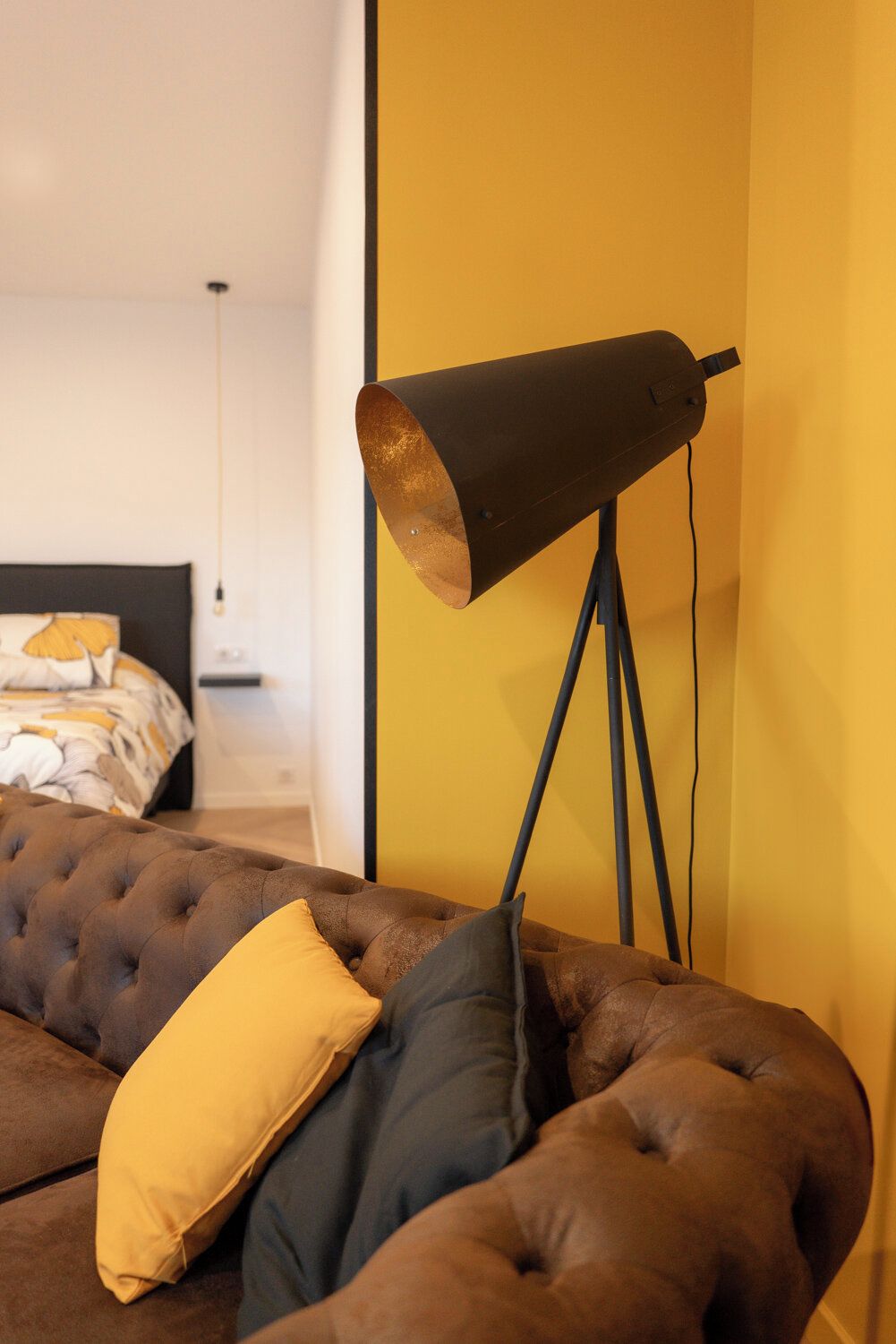 A modern bedroom with a tufted sofa, a floor lamp, and a bed with a patterned duvet.
