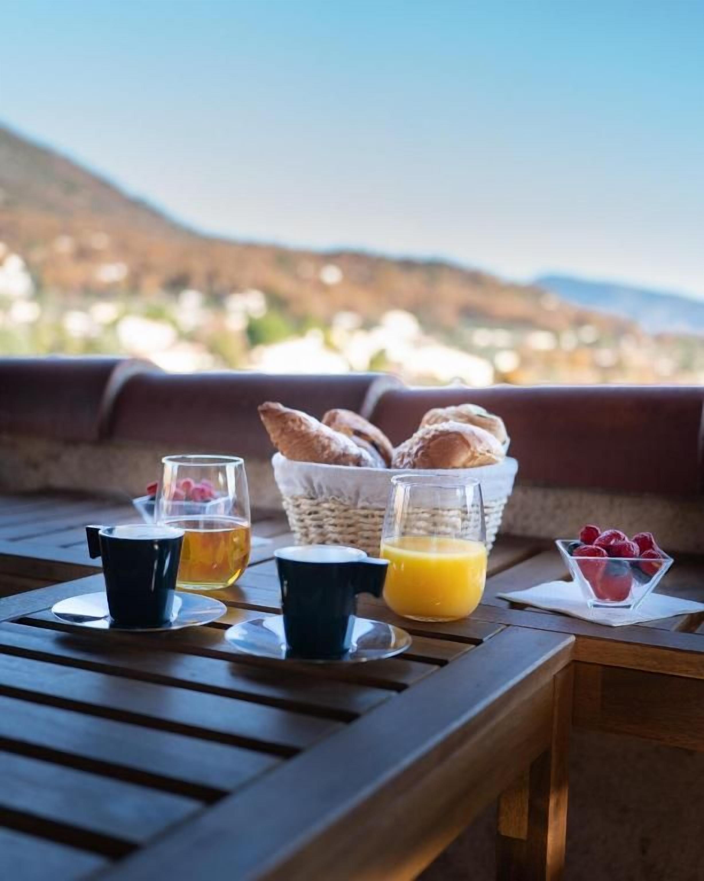 Frühstücksaufstellung mit Brot, Obst und Getränken auf einem Holztisch mit schöner Aussicht.