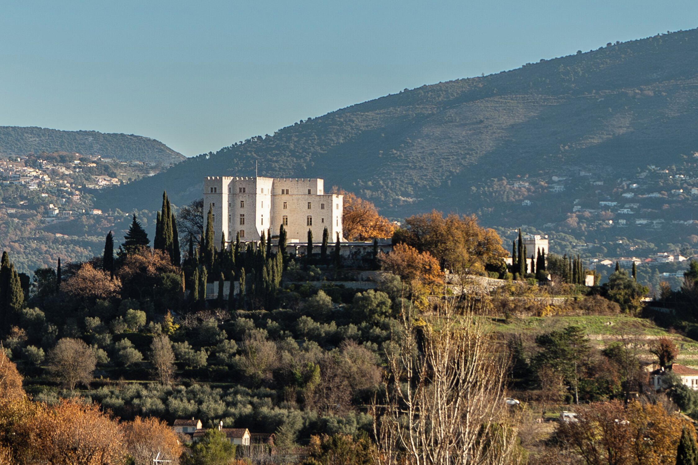 Un edificio simile a un castello su una collina, circondato da alberi e con vista panoramica su una cittadina.