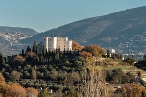 Un edifici semblant a un castell damunt d'un turó, amb arbres al voltant i una vista llunyana d'una vila.