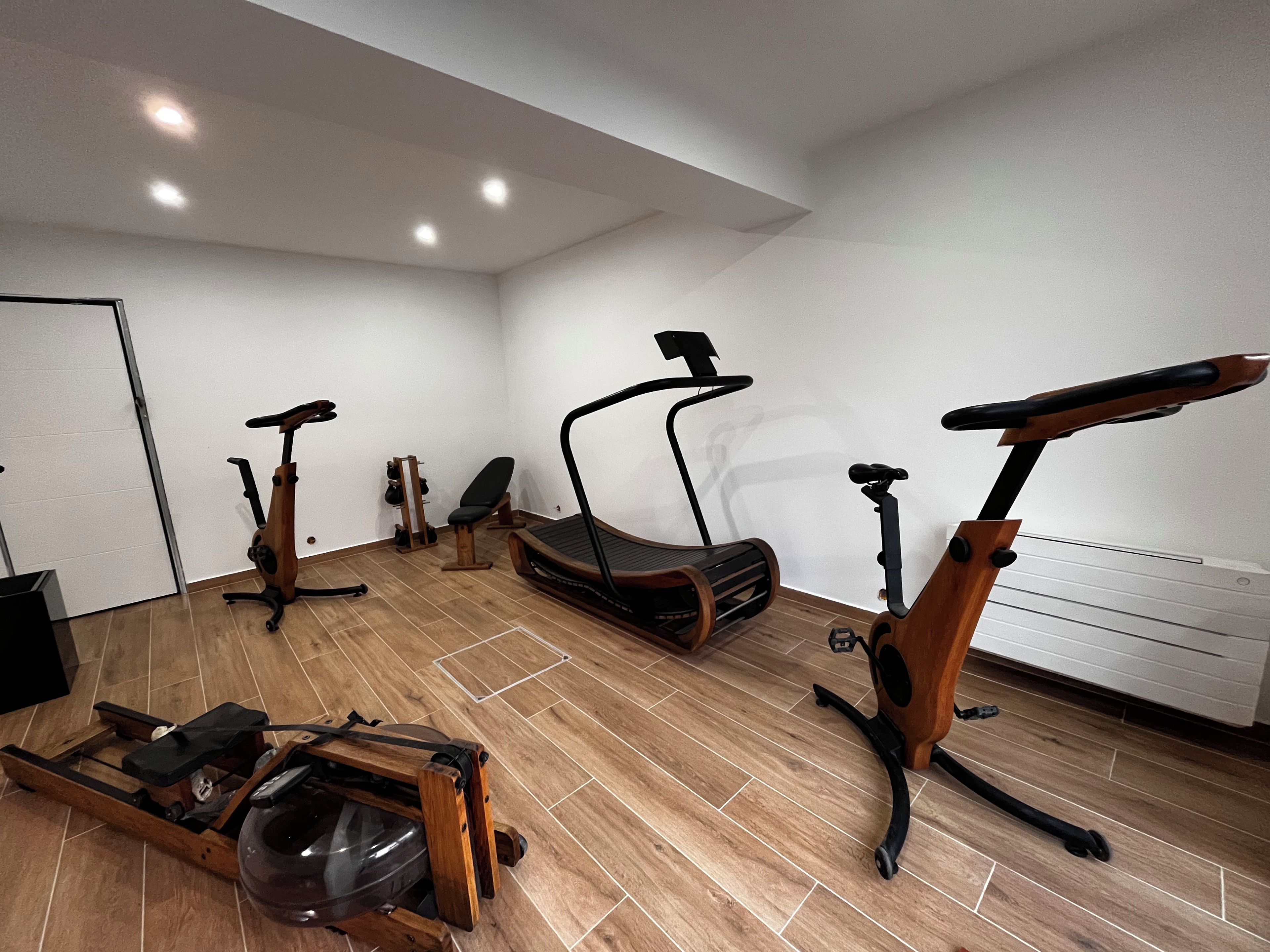 Un gimnasio moderno con equipo de ejercicio, incluyendo cintas de correr y bicicletas estáticas, suelo de madera e iluminación empotrada en el techo.