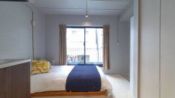 A bedroom with a bed, a bedside table, a window with curtains, and a view of the outside.
