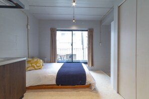 Ein Schlafzimmer mit Bett, Nachttisch, Fenster mit Vorhängen und Blick ins Freie.