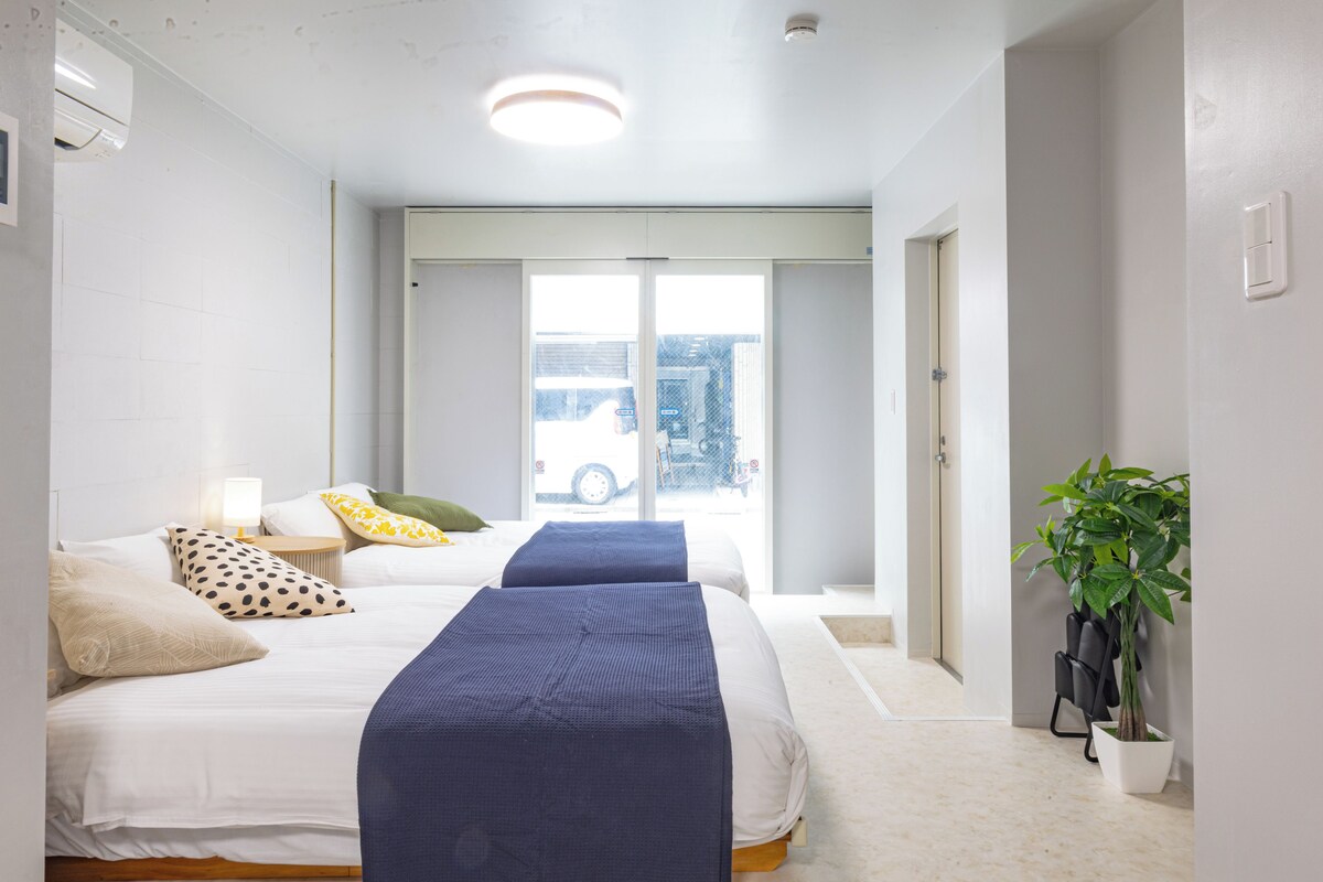 Ein Hotelzimmer mit zwei Betten, einer Zimmerpflanze und Blick auf die Straße.