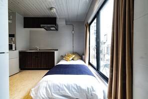 Ein kompaktes Hotelzimmer mit Bett, einer kleinen Küchenzeile und einem fenster mit Vorhängen.