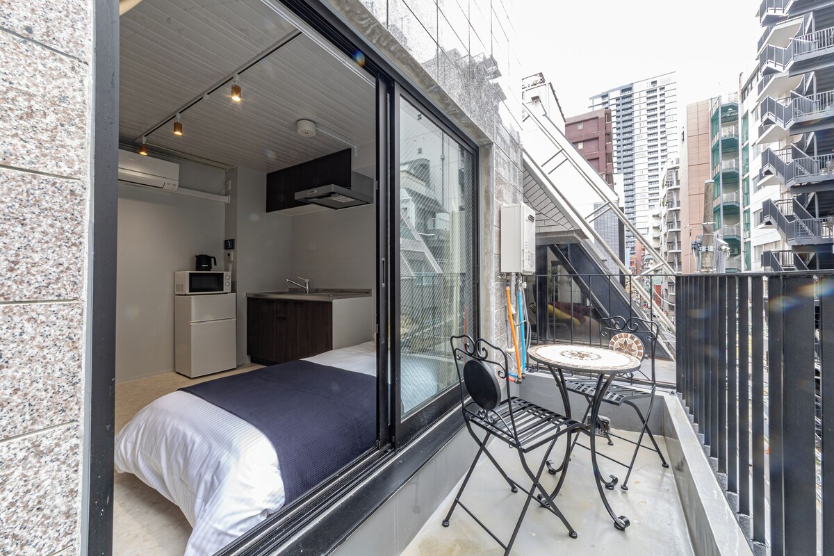 Eine moderne Wohnung mit Balkon, einem Bett, einer kleinen Küche und Blick auf die Stadt.