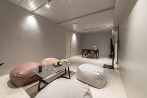Ein schlicht eingerichteter Raum mit Tisch, Stühlen, einem Sitzsack und einer kleinen Essecke.