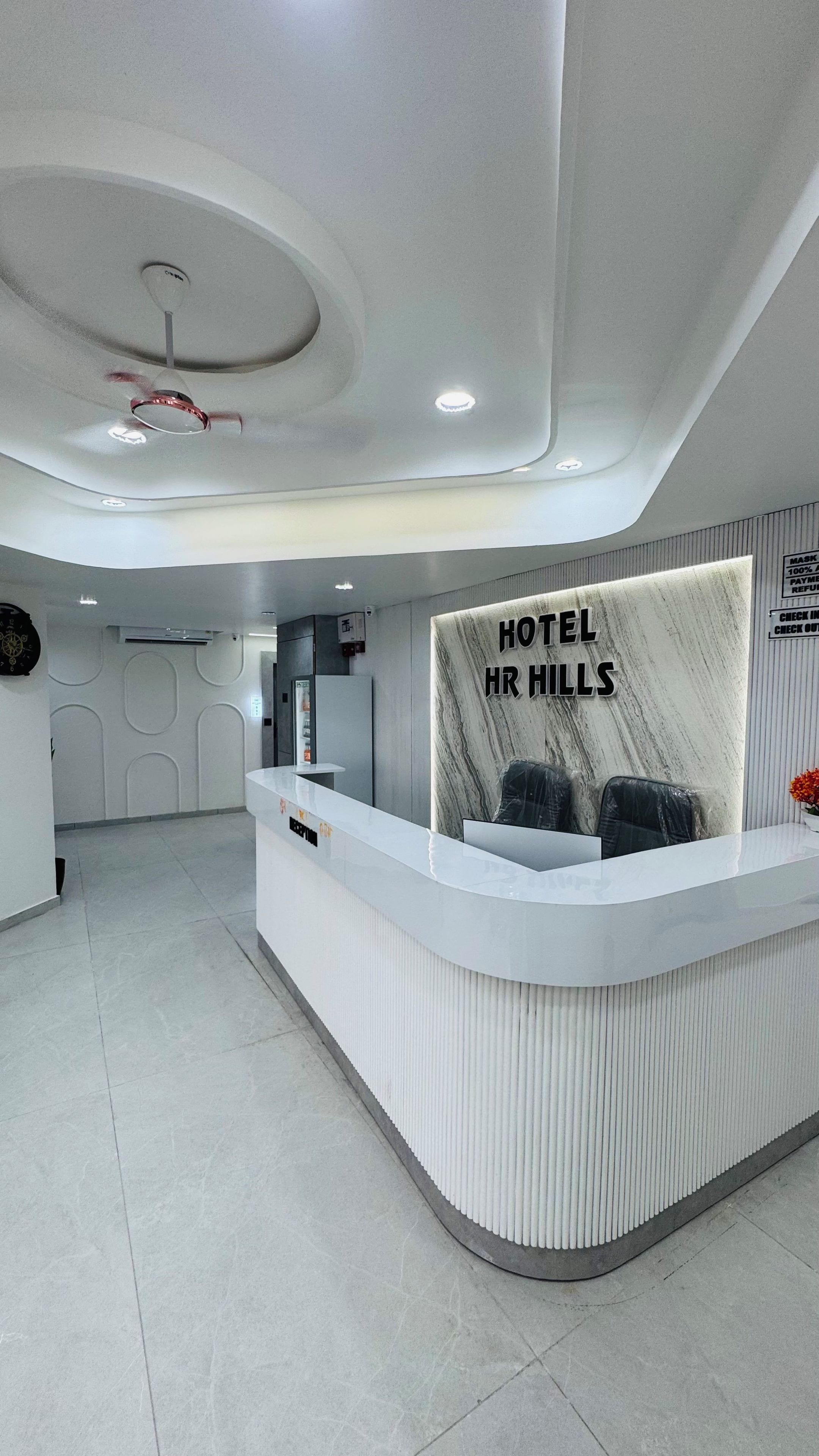 A hotel reception area with a marble counter, a ceiling fan, and a sign reading 'HOTEL HR HILLS'.