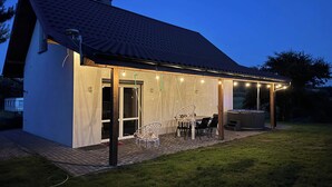 Et hus med en overdækket terrasse, udendørs møbler og et spabad.