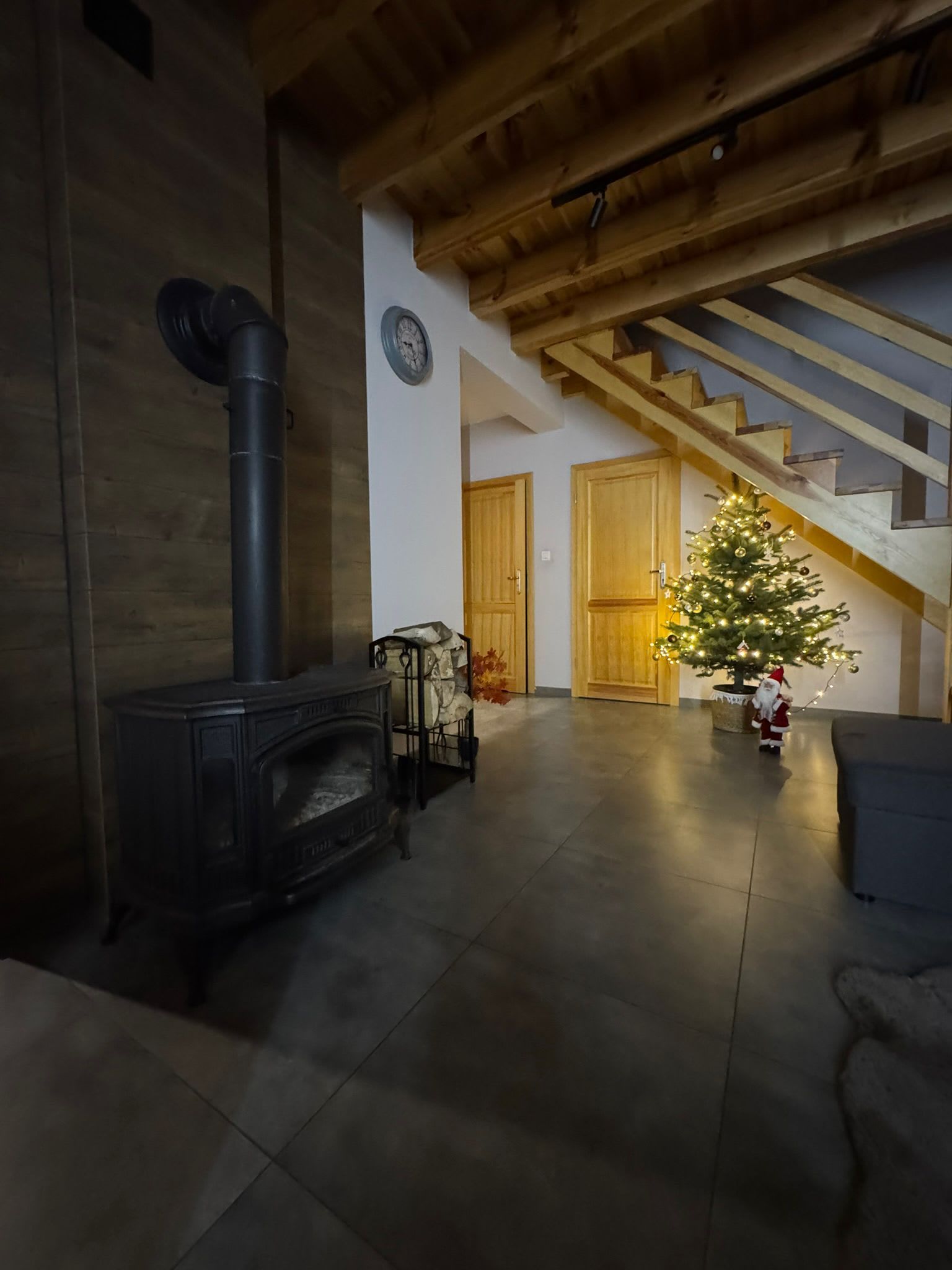 A room with a wood-burning stove, a staircase, and a decorated Christmas tree.