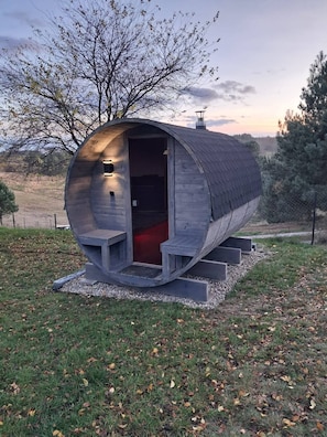 Una struttura di legno cilindrica con una porta, gradini che conducono ad essa e una piccola area esterna con una panchina.