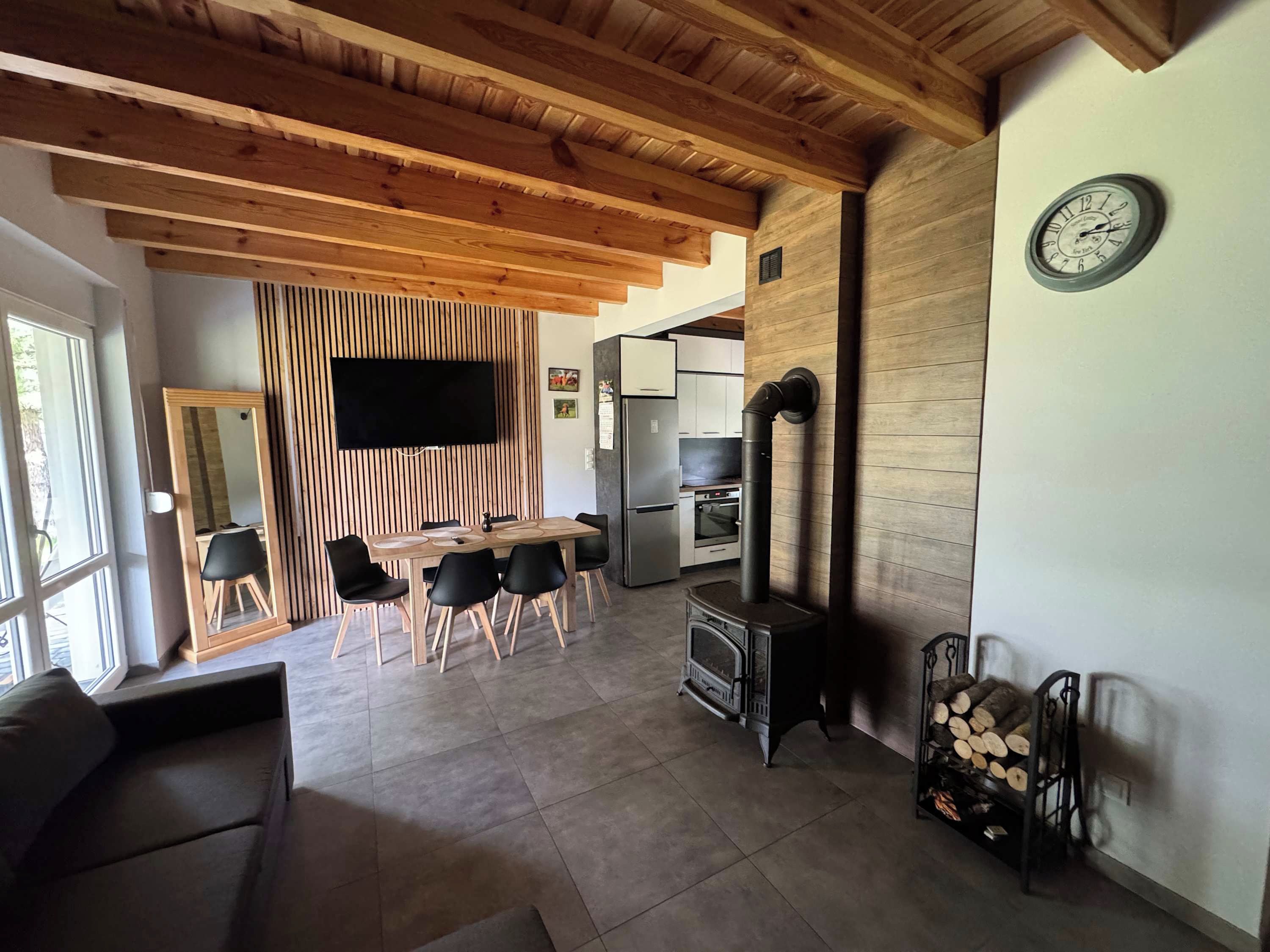 A modern kitchen with a built-in stove, wooden ceiling beams, and a dining area with a large mirror and black chairs.