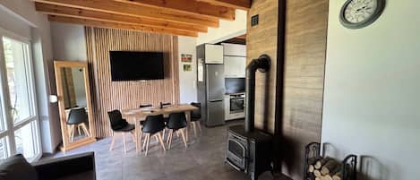 A modern kitchen with a built-in stove, wooden ceiling beams, and a dining area with a large mirror and black chairs.
