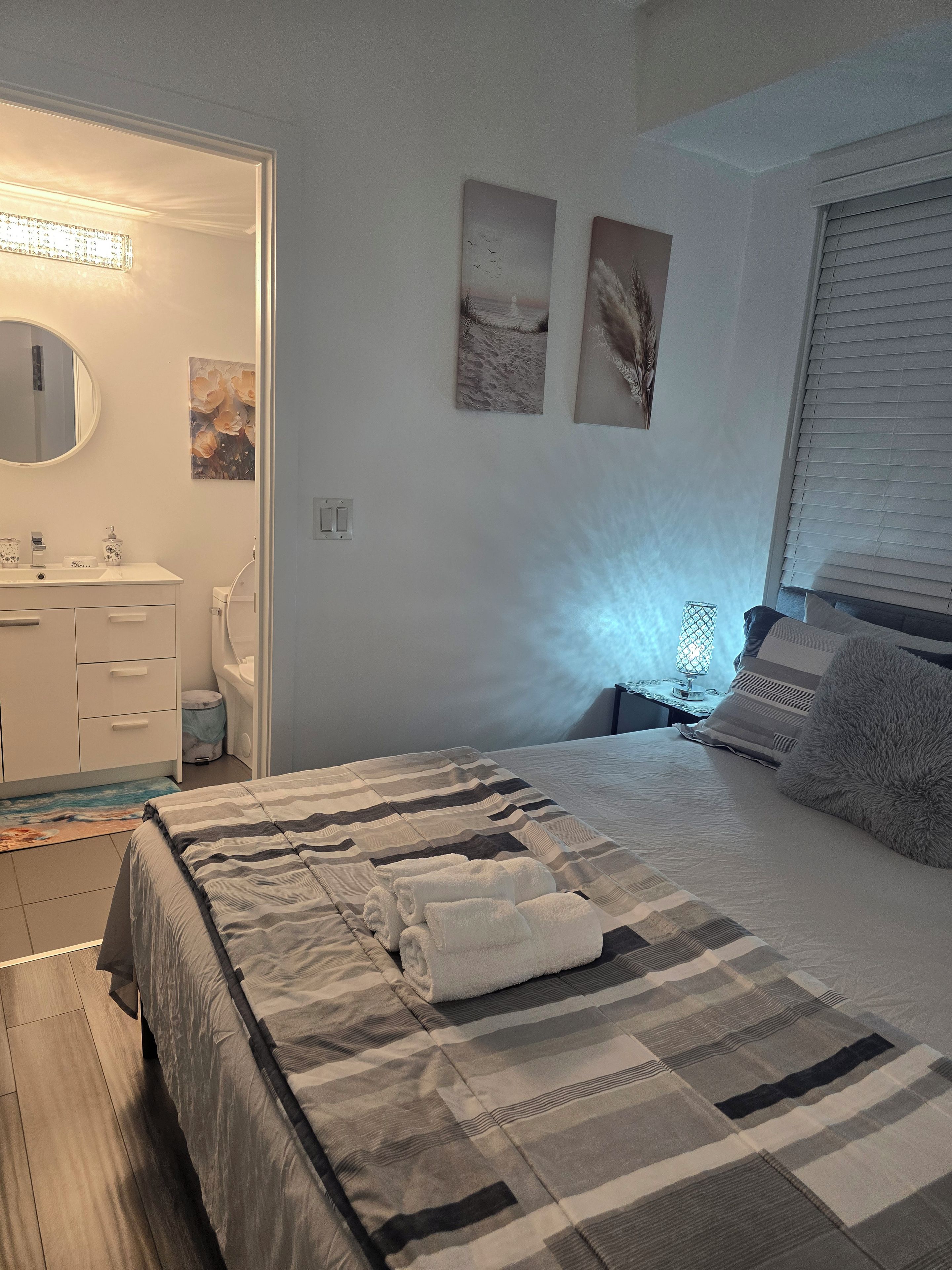 Un dormitorio con cama, mesita de noche, lámpara y ventana con persianas.