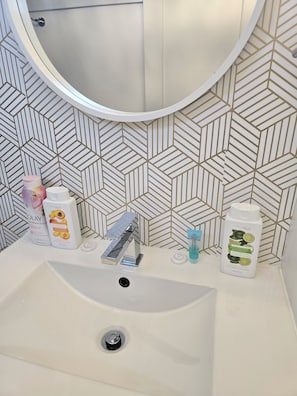 A bathroom sink with a modern faucet, a mirror, and toiletries on the countertop. - Niagara Bliss Relax Explore Repeat (Niagara Falls)