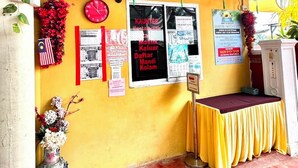 A yellow wall with multiple posters, a clock, and a small table with a yellow tablecloth.