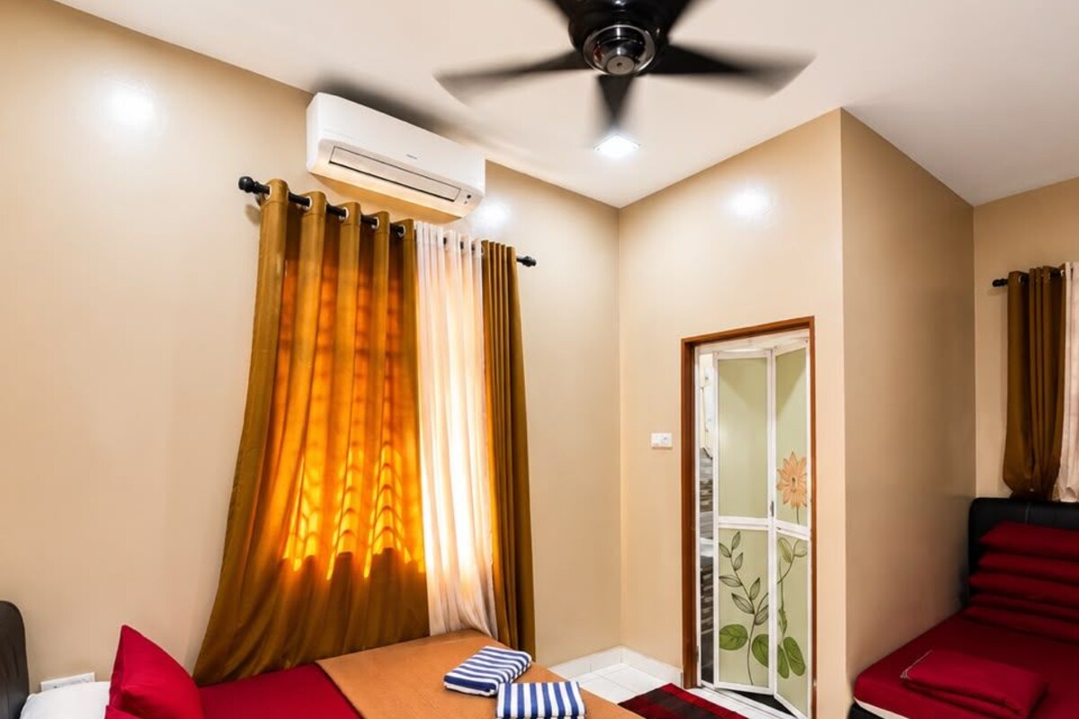 Une chambre d’hôtel avec un lit, un canapé rouge, un ventilateur de plafond, un appareil de climatisation et une fenêtre avec des rideaux.