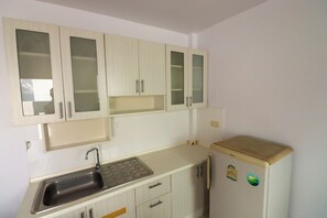 Una cocina con gabinetes blancos, un lavamanos de acero inoxidable y un refrigerador.