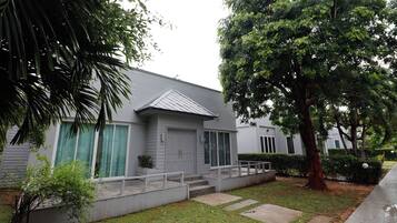 Uma casa com varanda, garagem e uma grande árvore no jardim.