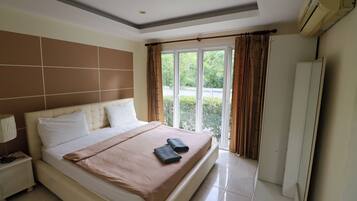 A hotel room with a large bed, a nightstand, a lamp, a wardrobe, and a window with curtains.