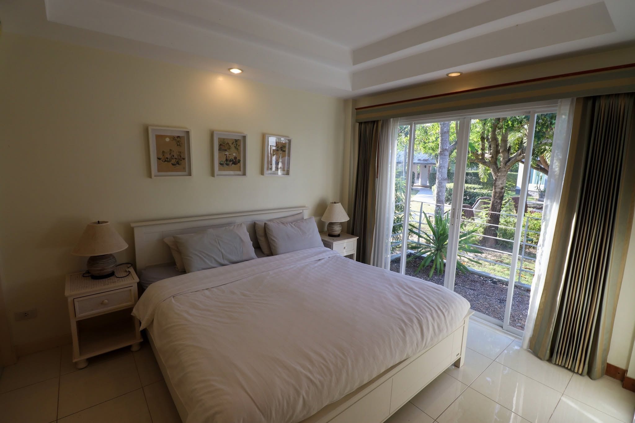 Un dormitorio con una cama grande, dos mesitas de noche y vistas a un jardín a través de un ventanal corredero.