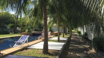 Un área de piscina con sillones reclinables, un sendero bordeado de palmeras y una piscina azul cristalina.