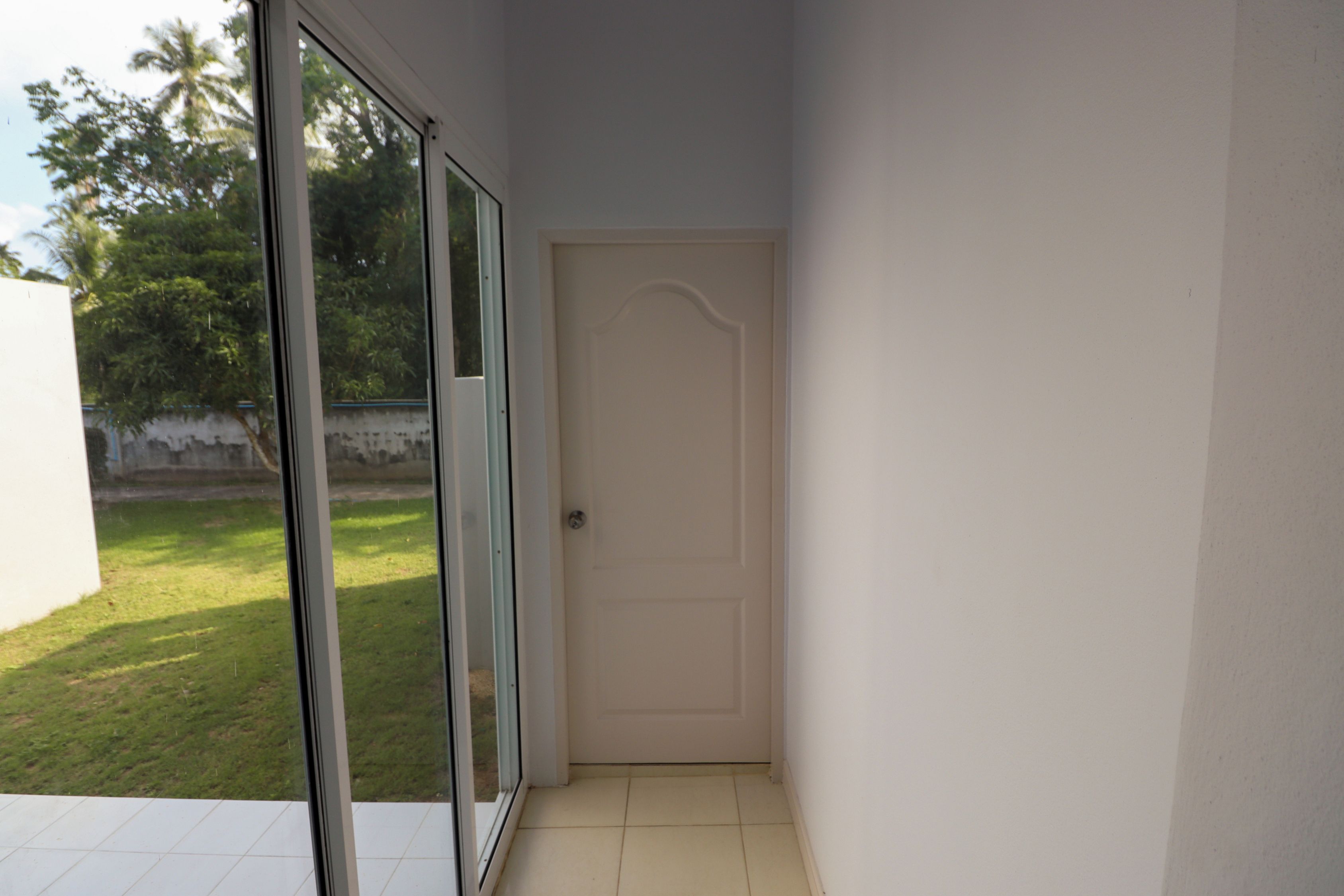 Ein Flur mit einer Schiebetür, die auf einen Balkon führt. Der Flur hat einen gefliesten Boden und eine schlichte weiße Wand.