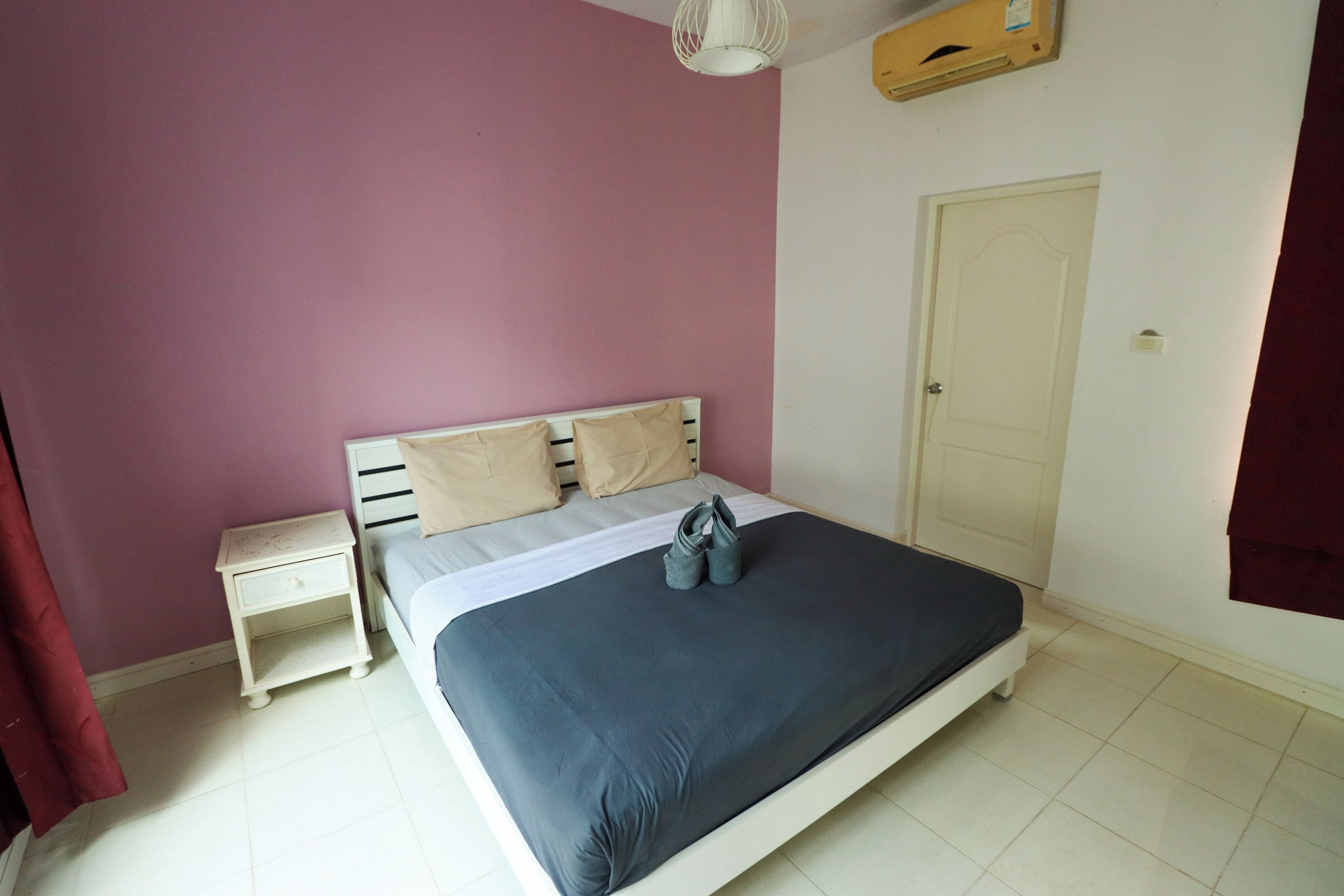 Un dormitorio con cama, mesita de noche, puerta y ventana con cortinas.