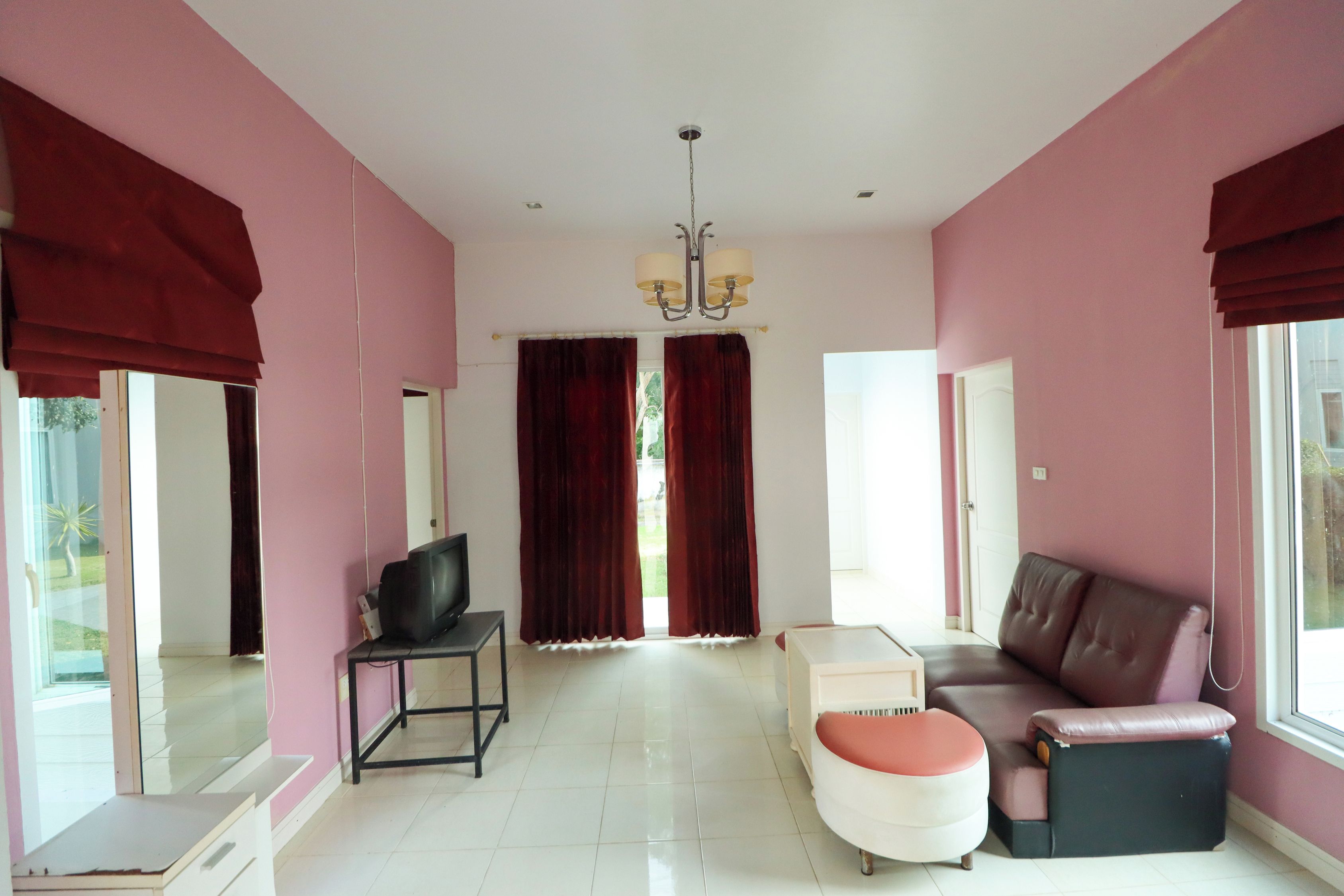 Amplia sala de estar con televisor sobre un mueble bajo, sofá, mesa de centro y un gran ventanal con cortinas.