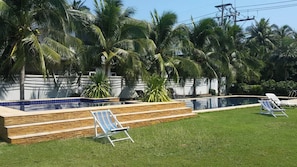 A swimming pool with a tiled edge, surrounded by a grassy area and palm trees.