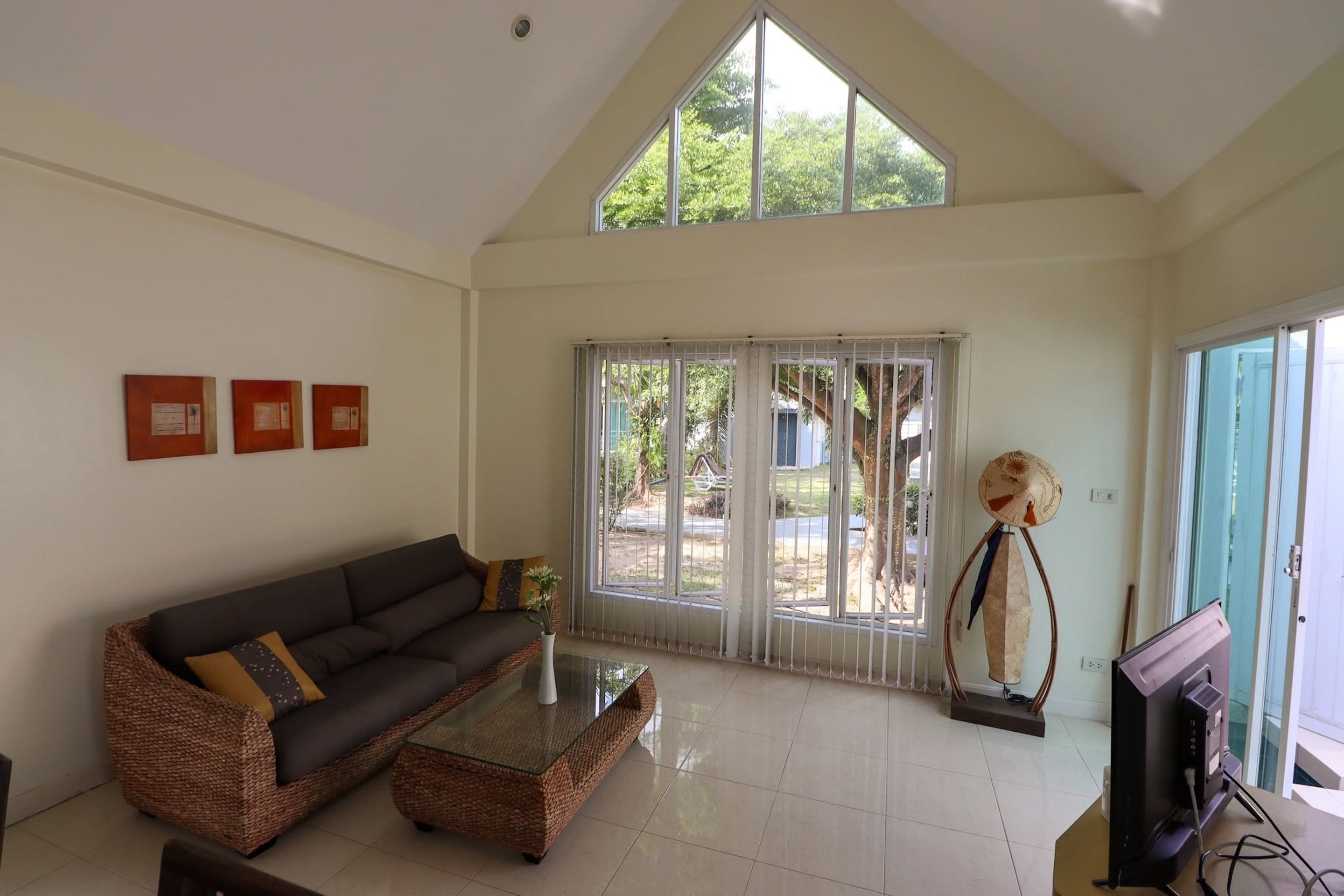 A spacious living room with a high ceiling, a dark-colored sofa, a glass coffee table, and a television.
