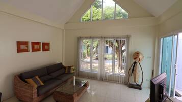 A spacious living room with a high ceiling, a dark-colored sofa, a glass coffee table, and a television.