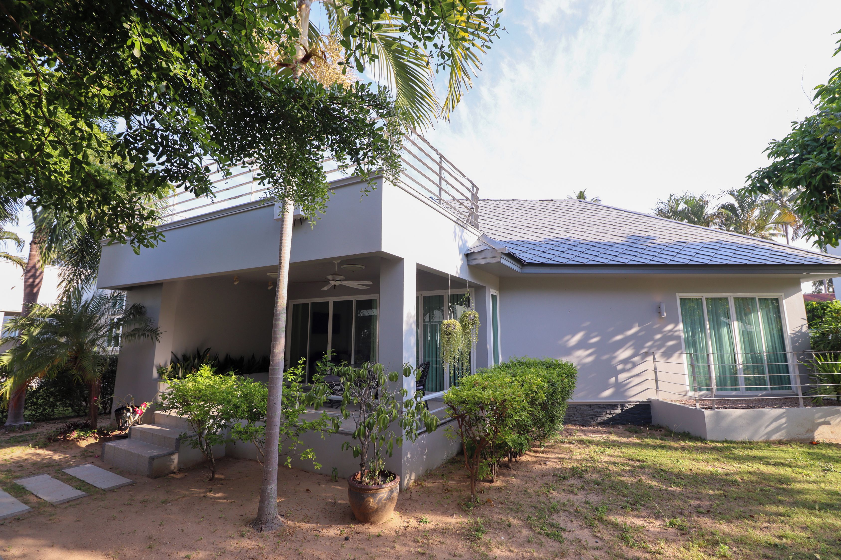 Una casa moderna de dos pisos con porche cubierto, paneles solares y un jardín bien cuidado.