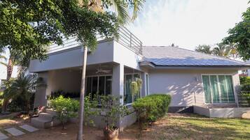Una casa moderna de dos pisos con porche cubierto, paneles solares y un jardín bien cuidado.
