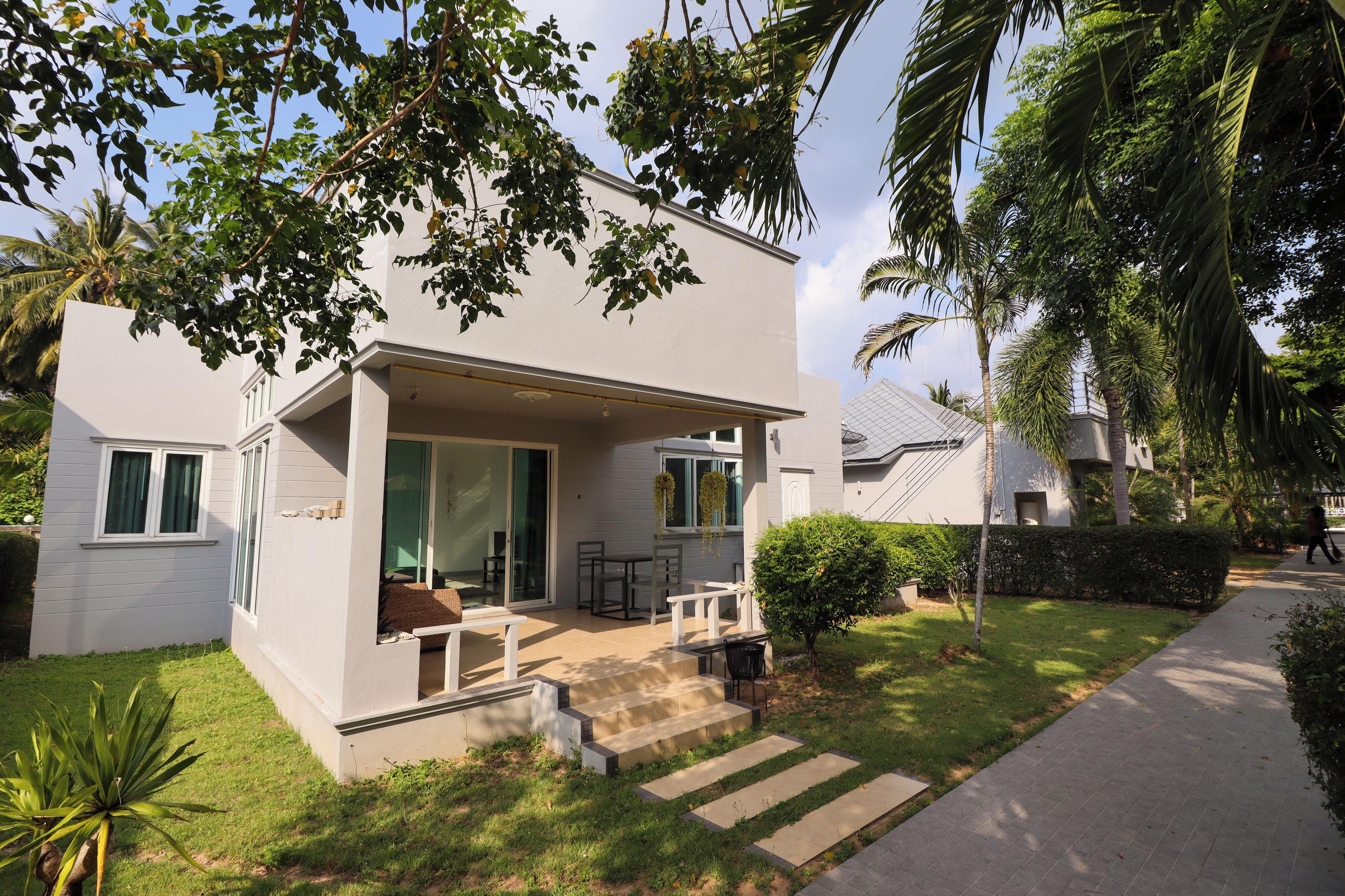 Uma casa moderna de dois andares com varanda coberta, um pequeno jardim e um acesso pavimentado.